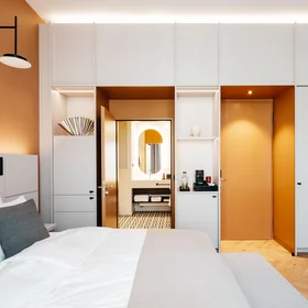 Ihr Stadthotel in Berlin: DASEYN | Fischerinsel Modernes Hotelzimmer mit weißem Bett, grauen Kissen und orangefarbenen Wänden